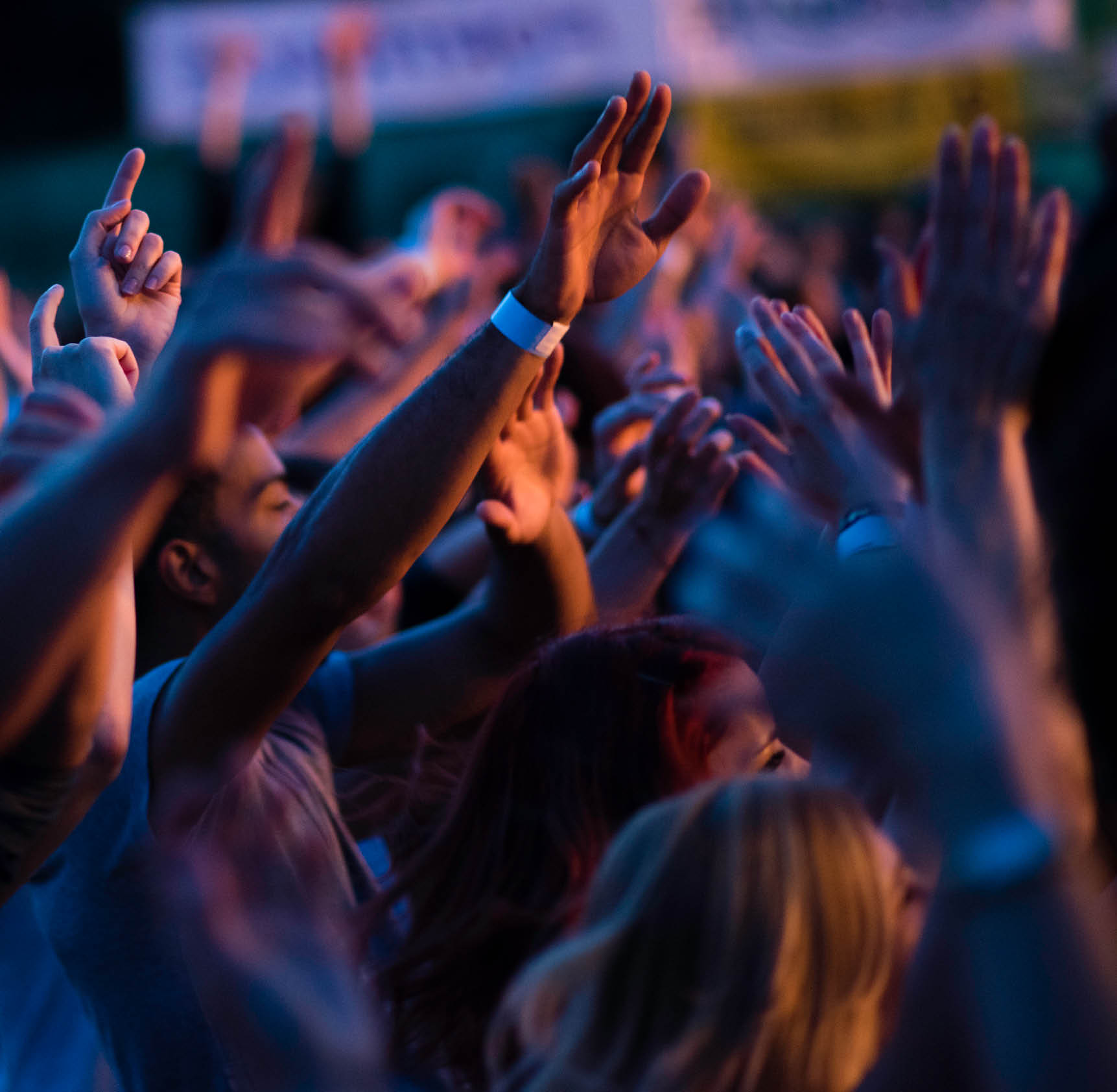 Group of people all looking in one direction with raised hands in the evening. At a concert or live DJ event.